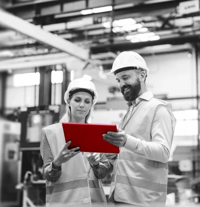 Two people wearing hard hats are positioned in front of a red tablet Two people wearing hard hats are positioned in front of a red tablet