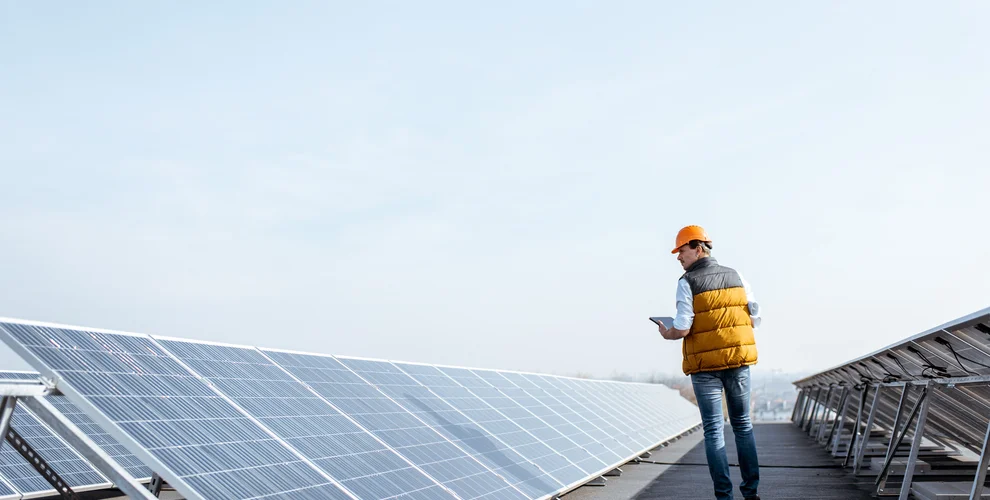 View on the rooftop solar power plant with mann walking and examining photovoltaic panels. Concept of alternative energy and its service